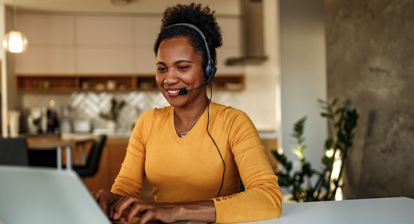Professional sitting at desk smiling representing how GoTo can support customers’ communication and remote support goals.