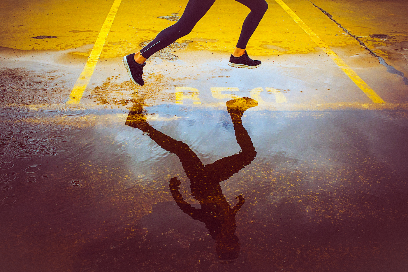 Person's leg and reflection running through a puddle in an empty parking lot at top speed
