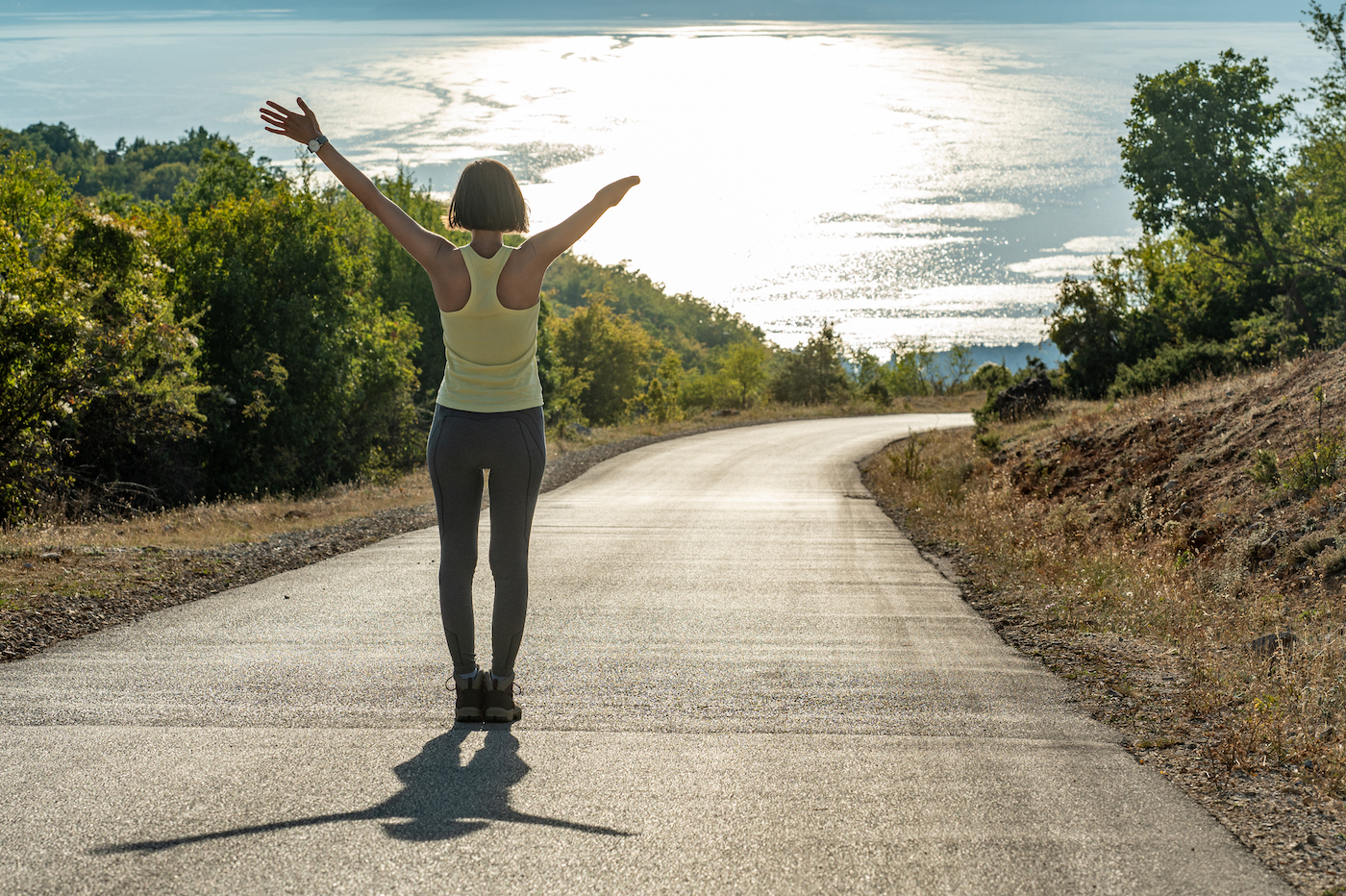 Happy woman with outstretched arms on a road overlooking a lake, representing how GoTo Resolve wins over the competition