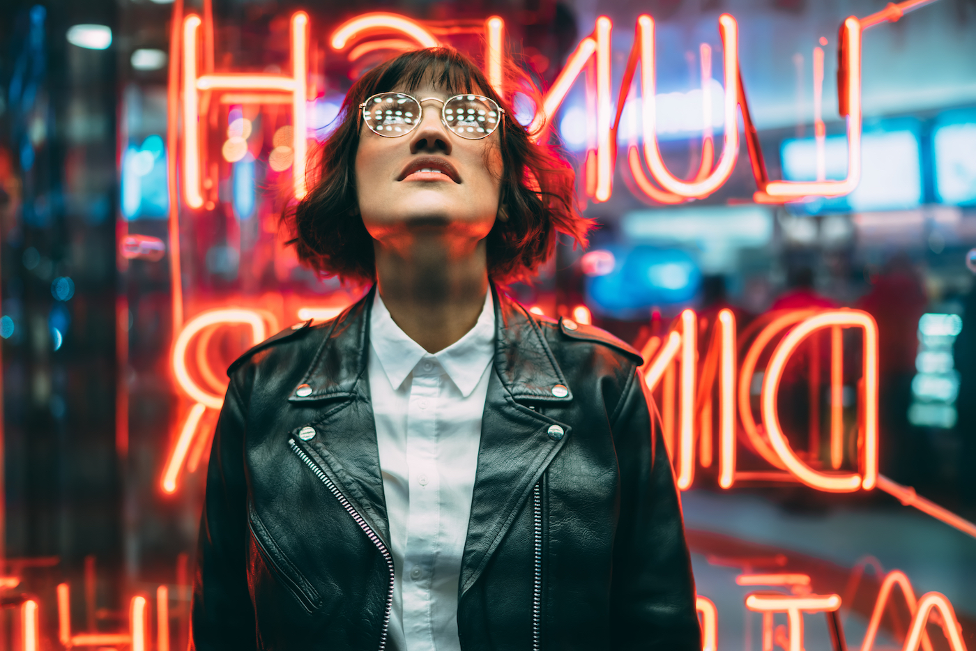 Woman standing in front of window with neon signage, looking upward and  enjoying a night out