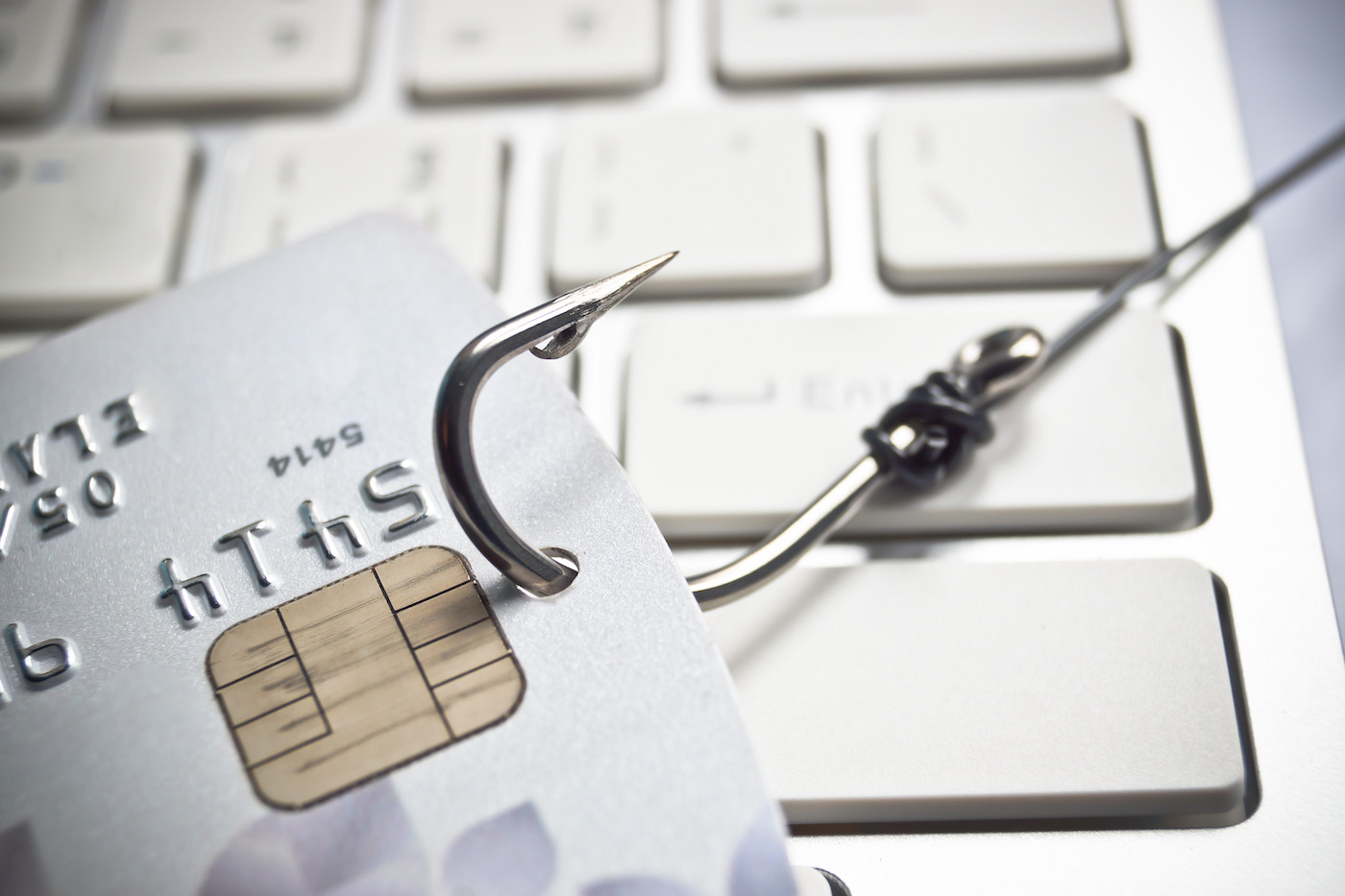Fish hook hooked onto a credit card on a computer keyboard, representing phishing and the importance of cyber security