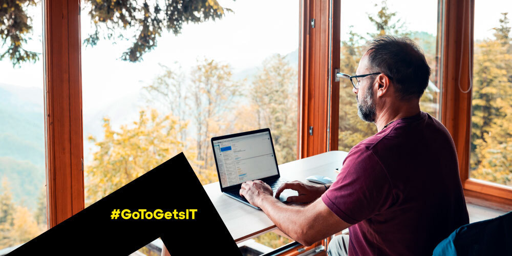 Man easily working on a laptop in a sunroom overlooking a scenic mountain forest with simple remote monitoring and management (RMM)