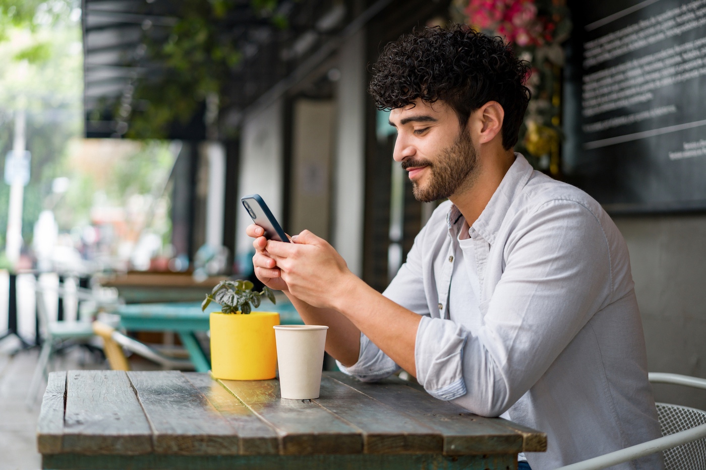 Remote worker using his smartphone at an outdoor café, highlighting the importance of mobile device management