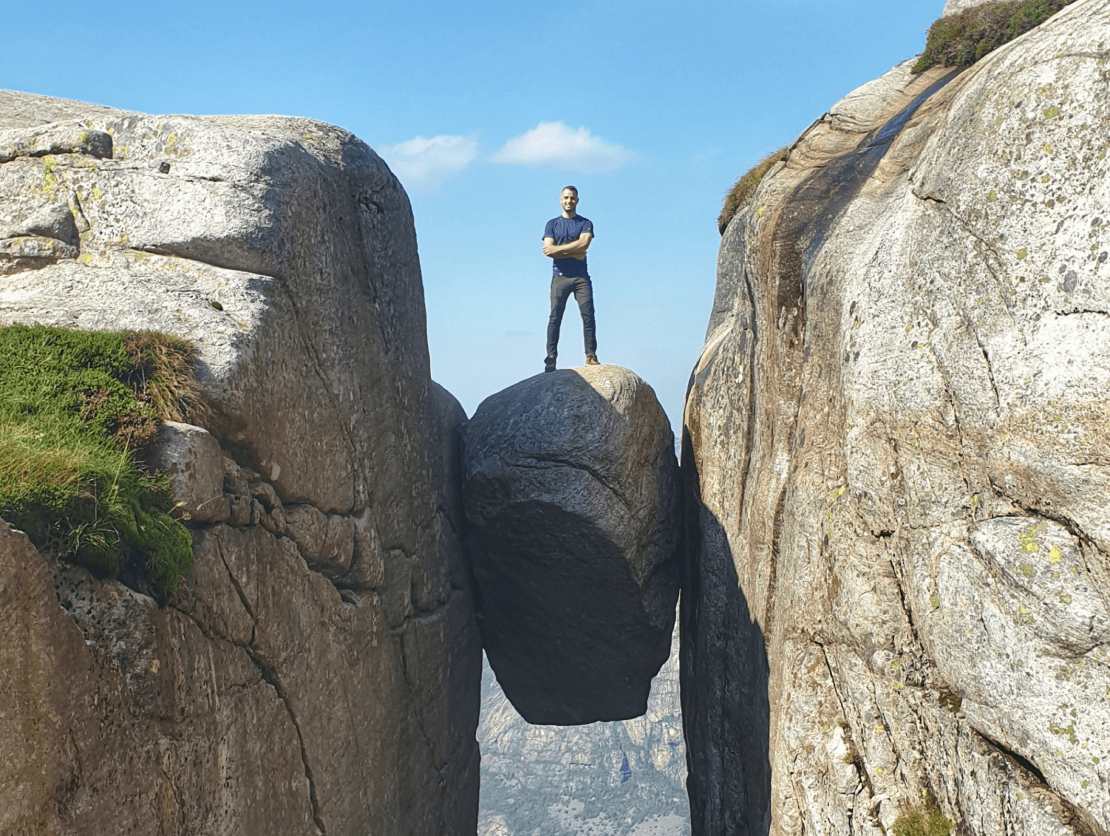 Eine Person steht mit verschränkten Armen zwischen zwei Felsklippen und sieht triumphierend aus.