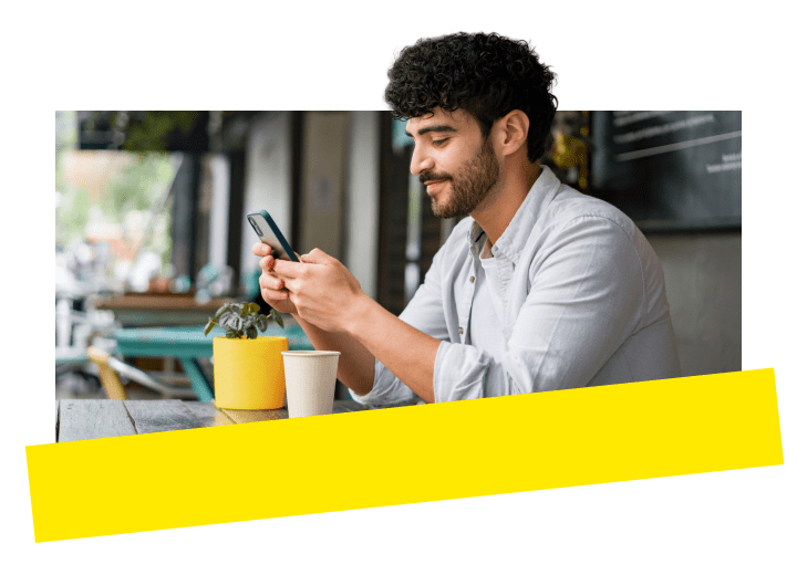 Profesional disfrutando del galardonado sistema de telefonía empresarial de GoTo en su dispositivo móvil mientras está sentado al aire libre en una cafetería.