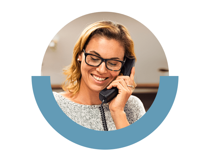 Lächelnde Mitarbeiterin tätigt mit GoTo Connect einen Anruf auf dem Tischtelefon